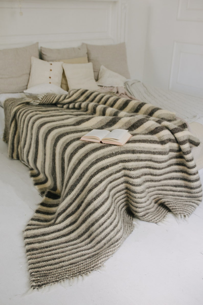 May include: A white bed with a striped gray and white blanket and a book on top. The bed has several pillows in various shades of beige and white.