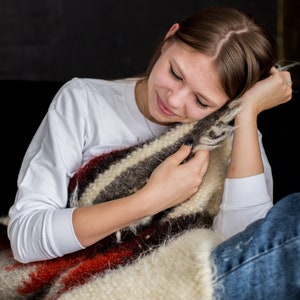May include: A young woman is sitting with a white long-sleeved shirt and blue jeans. She is holding a brown, white, and red striped blanket.