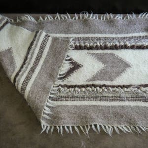 May include: A white and gray woven rug with a geometric pattern. The rug has a fringe border.