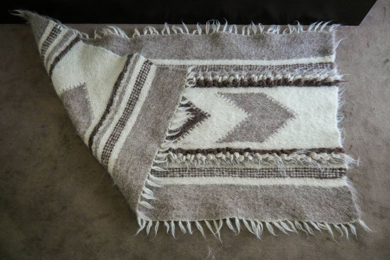 May include: A white and gray woven rug with a geometric pattern. The rug has a fringe border.