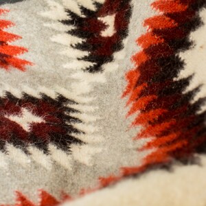 May include: A close-up of a white, gray, red, and brown woven blanket with a geometric pattern.