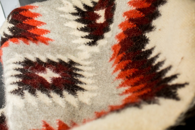 May include: A close-up of a white, gray, red, and brown woven blanket with a geometric pattern.