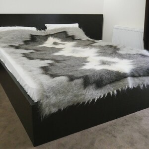 May include: A black bed frame with a white and gray sheepskin throw blanket. The blanket has a unique pattern and is soft and fluffy.
