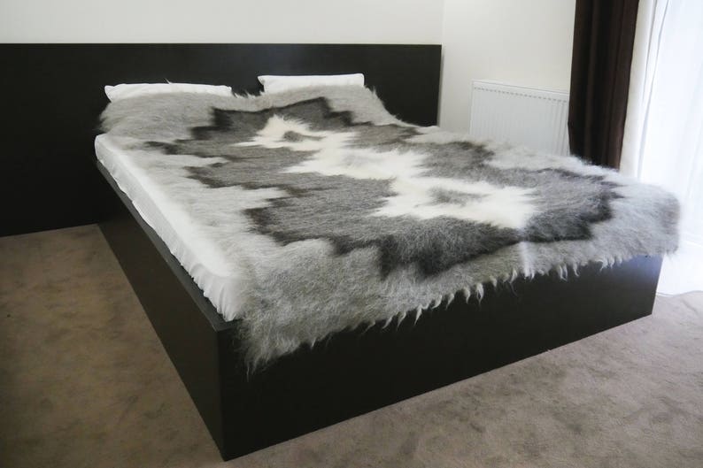 May include: A black bed frame with a white and gray sheepskin throw blanket. The blanket has a unique pattern and is soft and fluffy.