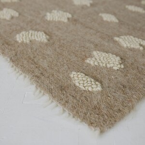 May include: A beige rug with a white, fluffy, cloud-like pattern. The rug has a fringe border.