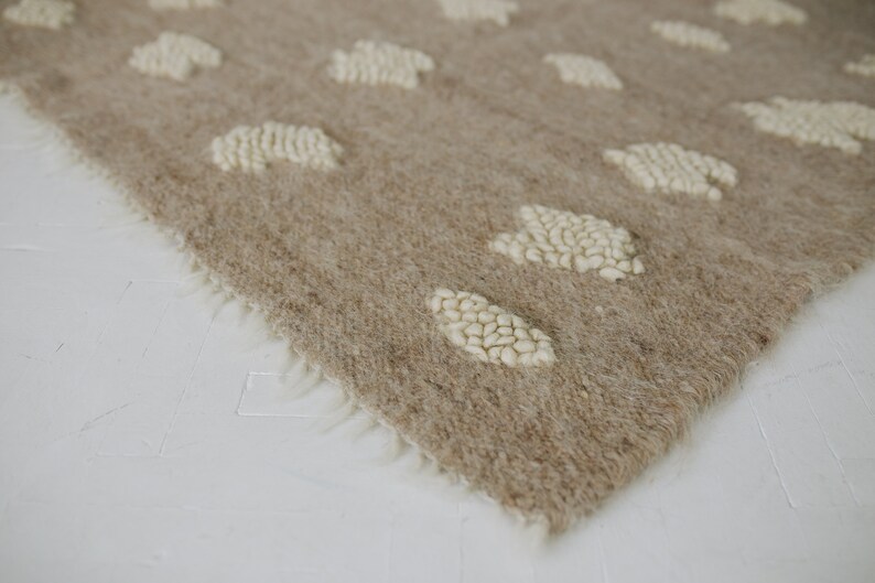 May include: A beige rug with a white, fluffy, cloud-like pattern. The rug has a fringe border.