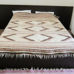 May include: A white bed with a brown and white patterned blanket. The blanket has a fringe around the edges.