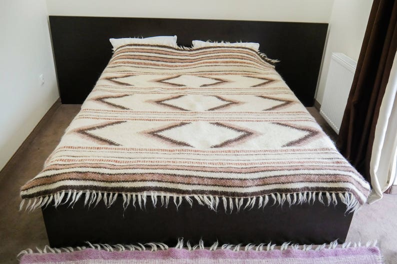 May include: A white bed with a brown and white patterned blanket. The blanket has a fringe around the edges.