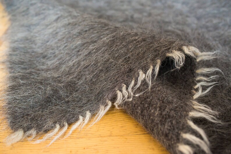 May include: Close-up of a dark gray and white fuzzy blanket with a frayed edge.