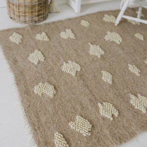 May include: A beige rug with a white, textured pattern of small circles. The rug has a fringe border and is laid out on a white floor.