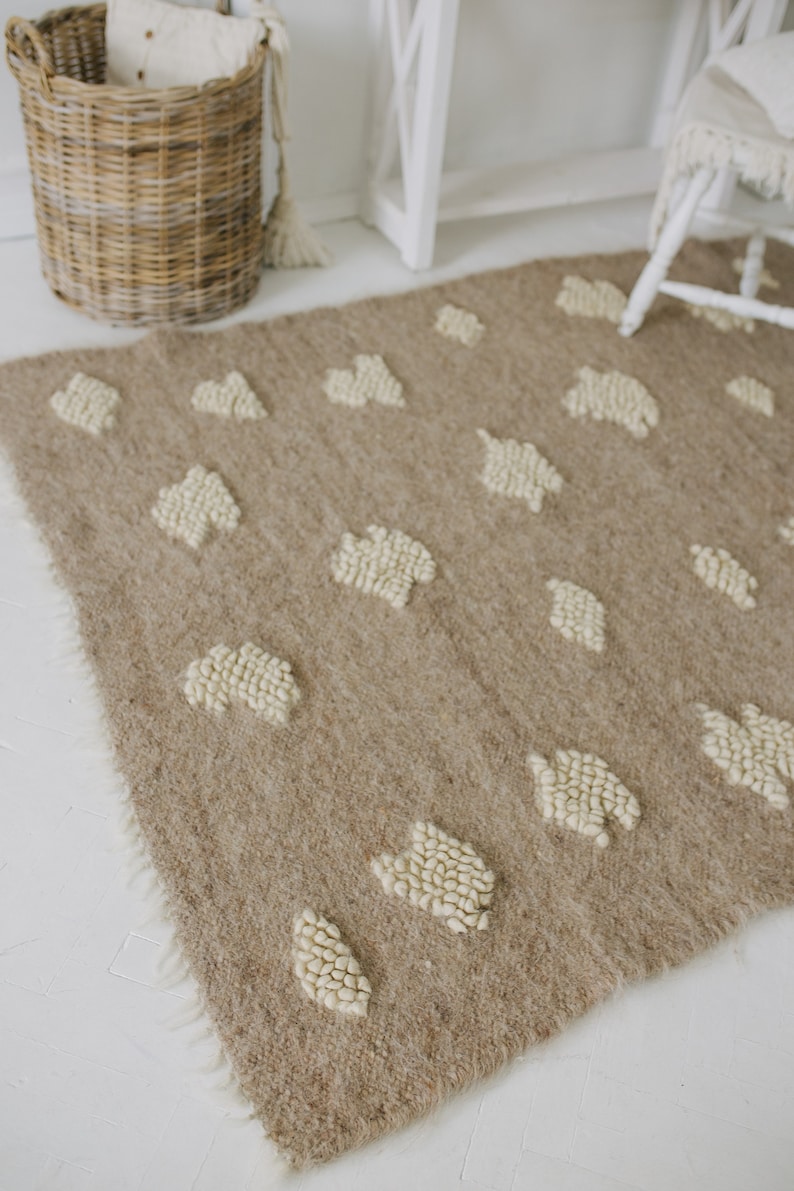 May include: A beige rug with a white, textured pattern of small circles. The rug has a fringe border and is laid out on a white floor.