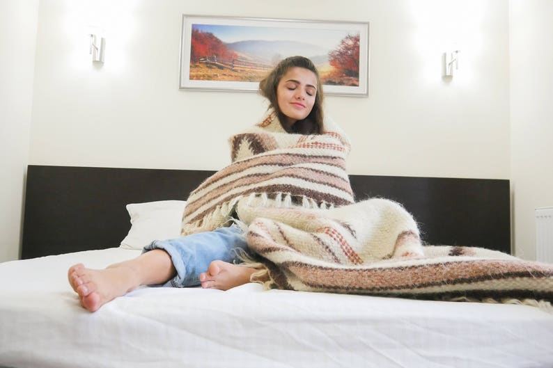 May include: A woman is wrapped in a white and brown striped blanket on a white bed. She is lying on her back with her eyes closed.
