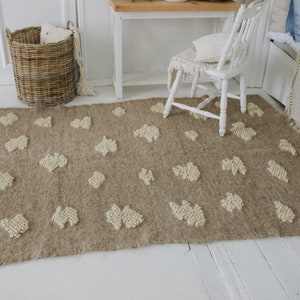 May include: A light brown rug with a white, fluffy, textured pattern. The rug has a fringe border and is laid out on a white wooden floor.