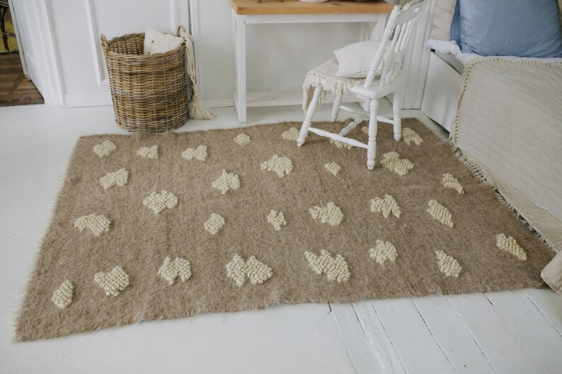 May include: A light brown rug with a white, fluffy, textured pattern. The rug has a fringe border and is laid out on a white wooden floor.