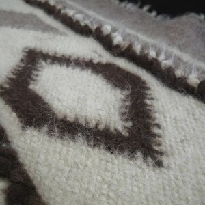 May include: A close-up of a white and brown woven fabric with a diamond pattern. The fabric is soft and fuzzy, and the diamond pattern is created by the different colors of the yarn.