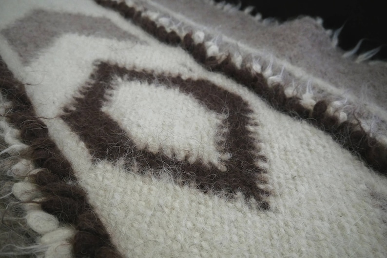 May include: A close-up of a white and brown woven fabric with a diamond pattern. The fabric is soft and fuzzy, and the diamond pattern is created by the different colors of the yarn.