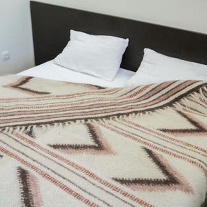 May include: A white bed with a brown headboard and two white pillows. A white and brown patterned blanket is draped over the bed.