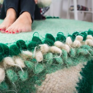 May include: A green and white fluffy rug with a fringe border. The rug has a textured surface and is made of wool.
