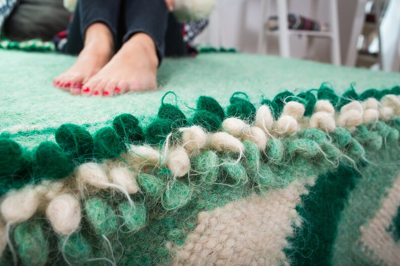 May include: A green and white fluffy rug with a fringe border. The rug has a textured surface and is made of wool.