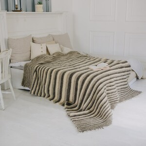 May include: A white bed with a striped throw blanket and a book on top. The blanket has a fringe edge and is made of a soft, fluffy material.