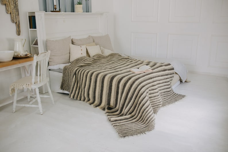 May include: A white bed with a striped throw blanket and a book on top. The blanket has a fringe edge and is made of a soft, fluffy material.