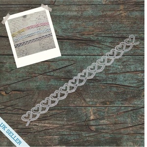 May include: A silver heart-shaped trim with a repeating pattern of hearts. The trim is displayed on a wooden surface.