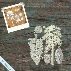 May include: Metal die cuts for crafting, featuring a set of pine trees and pine cones. The die cuts are silver in colour and are shown on a wooden background.