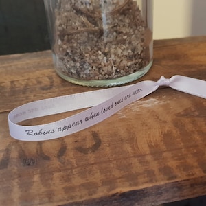 Op de afbeelding: Een lichtpaars lint met de tekst "Robins appear when loved ones are near" erop gedrukt.