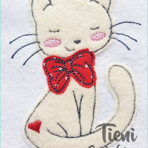 Könnte beinhalten: Eine weiße Filzkatze mit einer roten Schleife und geschlossenen Augen. Die Katze sitzt auf einem weißen Hintergrund mit dem Text "Tieni Schleichen" darunter.