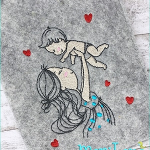 Könnte beinhalten: Stickerei mit einer Mutter, die ein Baby in die Luft hält. Die Mutter hat lange schwarze Haare und trägt ein blaues und weißes gepunktetes Kleid. Das Baby trägt eine weiße Windel und hat kurze braune Haare. Um das Motiv herum sind rote Herzen verteilt. Der Text "mariLena Stoffzauberereien" befindet sich am unteren Rand des Motivs.