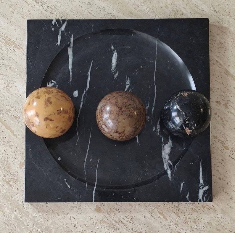 May include: A black marble tray with a rounded edge and three decorative spheres. The spheres are made of different types of marble, one is brown and white, one is black and white, and one is tan and brown.