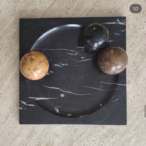 May include: A black marble tray with a circular indentation and three round spheres. The spheres are black, brown, and beige.
