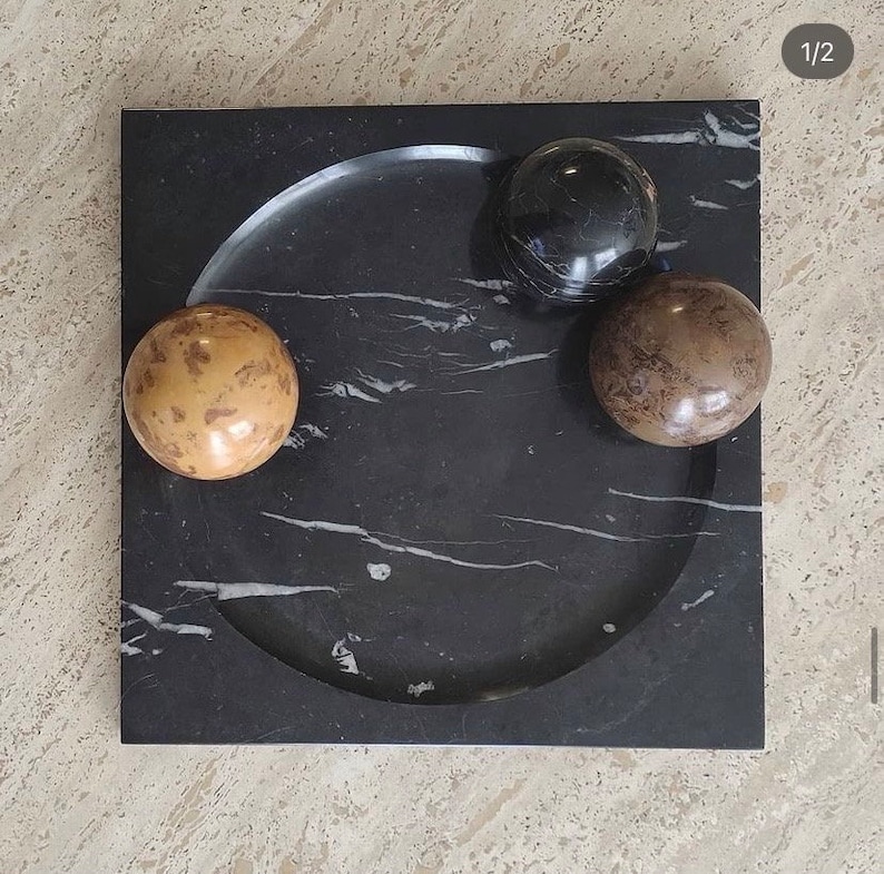 May include: A black marble tray with a circular indentation and three round spheres. The spheres are black, brown, and beige.