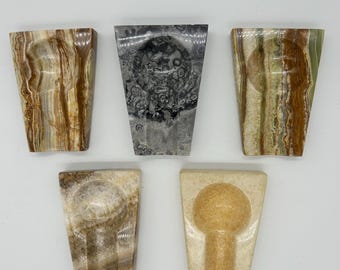 May include: Five different marble ashtrays in various colors and patterns. The ashtrays are all triangular in shape and have a small indentation in the center for holding cigarettes.