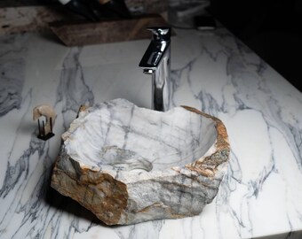 Può includere: Un lavabo in marmo bianco scolpito da una grande roccia con un rubinetto cromato. Il lavabo è su un piano di lavoro in marmo bianco.