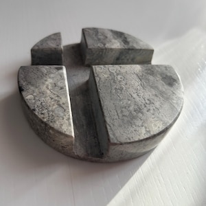 May include: A round, gray marble phone stand with four sections. The stand is made of natural stone with a unique pattern.
