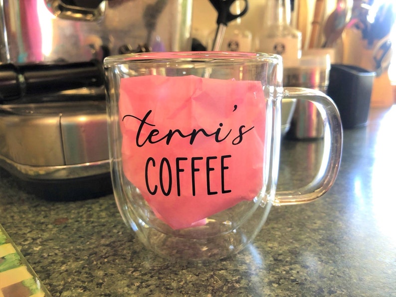 May include: A clear glass double-walled mug with a pink paper liner that says "Terri's Coffee" in black lettering.