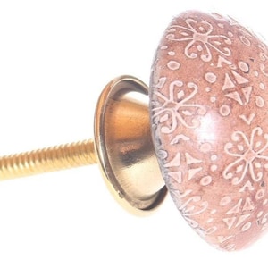 Pode incluir: Um botão de armário de cerâmica rosa com um padrão floral branco e um parafuso de metal dourado.