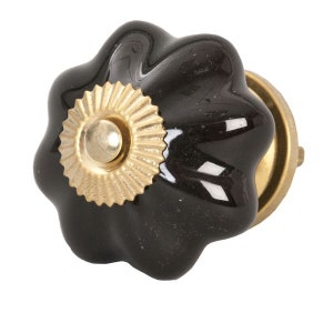Puede incluir: Pomo de armario de cerámica negra con un acento de metal dorado. El pomo tiene un diseño festoneado y un centro elevado.
