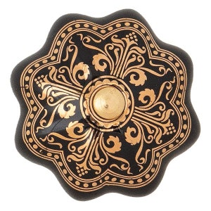 Peut inclure: Un bouton de meuble décoratif noir et doré avec un motif floral. Le bouton a un bord festonné et un centre doré. Le motif doré est gravé dans la surface noire.