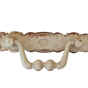 Może przedstawiać: Biały, metalowy klamka do drzwi z ozdobnymi detalami i wykończeniem w stylu vintage. Klamka ma zaokrąglony, owalny kształt z wypukłym środkowym elementem.