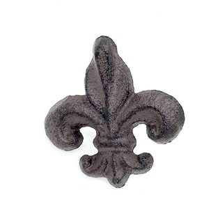Puede incluir: Un adorno de flor de lis de color marrón oscuro y texturizado con una apariencia de metal fundido rugoso. El objeto presenta un pétalo central vertical flanqueado por dos pétalos laterales curvos y una sección base más pequeña, todo en un diseño simétrico.