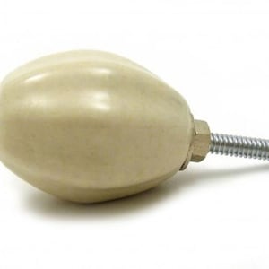 Op de afbeelding: Een crèmekleurige keramische kastknop met een zilveren schroef. De knop heeft de vorm van een afgeronde ovaal met een getextureerd oppervlak.