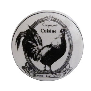 Pode incluir: Puxador de armário redondo em cerâmica branca com uma ilustração a preto e branco de um galo. As palavras "Organic Cuisine" e "Bistro Le Coq" estão impressas no puxador. O desenho é emoldurado por uma borda decorativa.