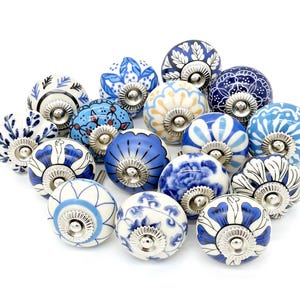 Puede incluir: Una colección de pomos redondos de cerámica para armarios con varios patrones en azul y blanco, incluyendo diseños florales, geométricos y de hojas. Cada pomo tiene una base de metal plateado y un tornillo central para su montaje.