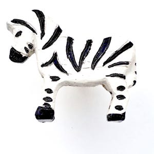 Op de afbeelding: Witte keramische zebra-figuur met zwarte strepen en vlekken. De zebra staat op alle vier poten met zijn hoofd gedraaid naar de zijkant.