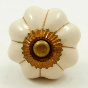 Pode incluir: Um botão de armário de cerâmica branca com um centro dourado e um design em forma de flor. O botão tem um centro elevado e um acabamento liso e brilhante.