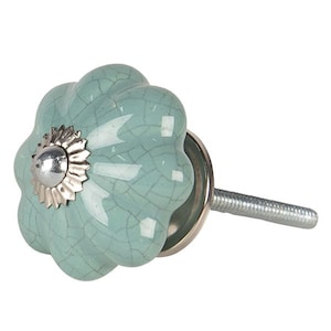 May include: A decorative cabinet knob with a light teal, flower-shaped ceramic head. The knob features a crackle glaze finish, a silver-colored metal base, and a threaded screw for installation. The knob's head measures approximately 2 inches in diameter.