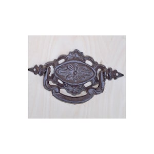 Könnte beinhalten: Ein Schubladenzug aus Gusseisen mit einem verzierten Design. Der Zug ist dunkelbraun und hat ein Blumenmuster.