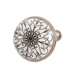 Könnte beinhalten: Ein weißer Keramik-Schrankknauf mit einem silbernen Metallsockel. Der Knauf zeigt ein kompliziertes schwarz-weißes Design aus wirbelnden Linien und einem zentralen Kreismotiv.